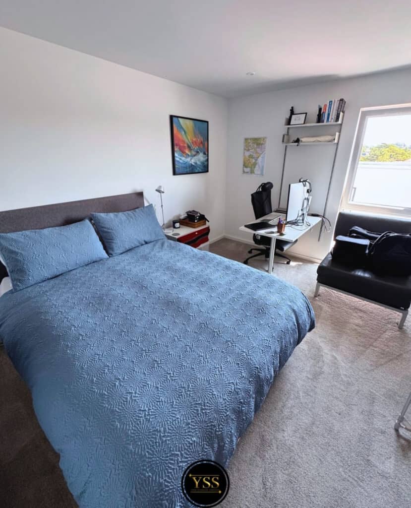 Bright clean bedroom with blue bedspread and modern workspace, perfect for comfort and productivity.