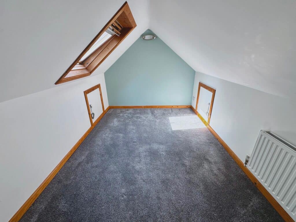 Clean, freshly painted attic room with skylight, wooden trims, and new carpet flooring. Perfect for home renovation and painting services.
