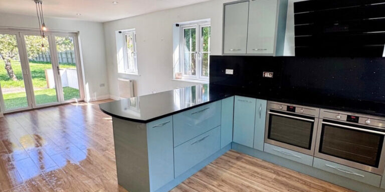 Bright modern kitchen with blue cabinets, black countertops, and wood flooring, showcasing professional cleaning.