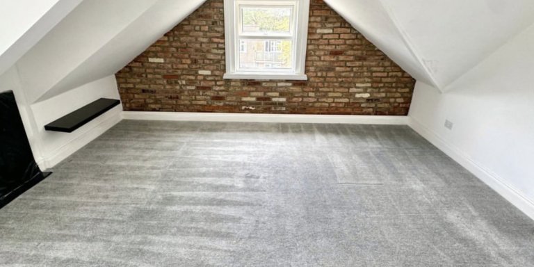 Bright renovated attic room with brick feature wall, carpet flooring, double-glazed window, ideal for home office or storage.